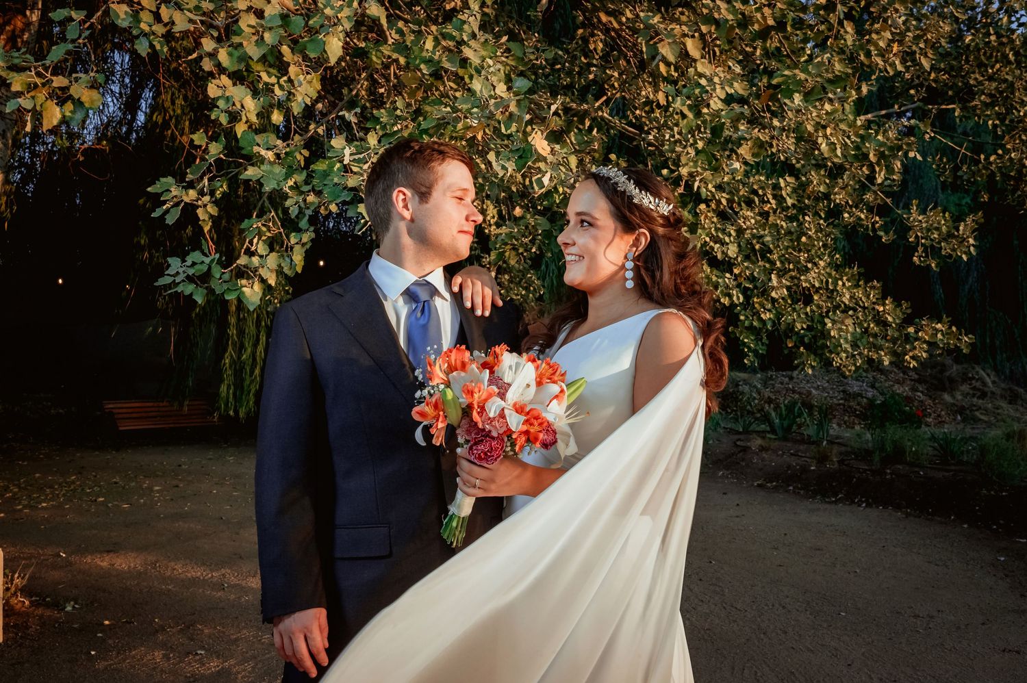 Bride and groom gazing at each other under glowing golden trees at twilight.