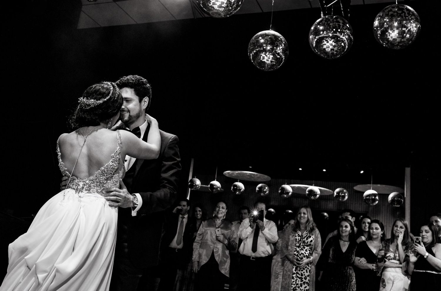 Bride and groom share intimate first dance while wedding guests watch and applaud in background.