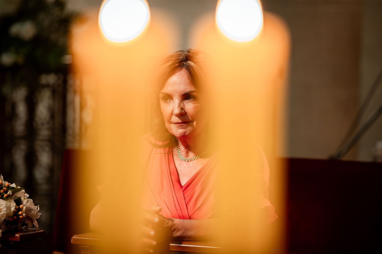 Woman in pink dress viewed through glowing candles during romantic church wedding ceremony.