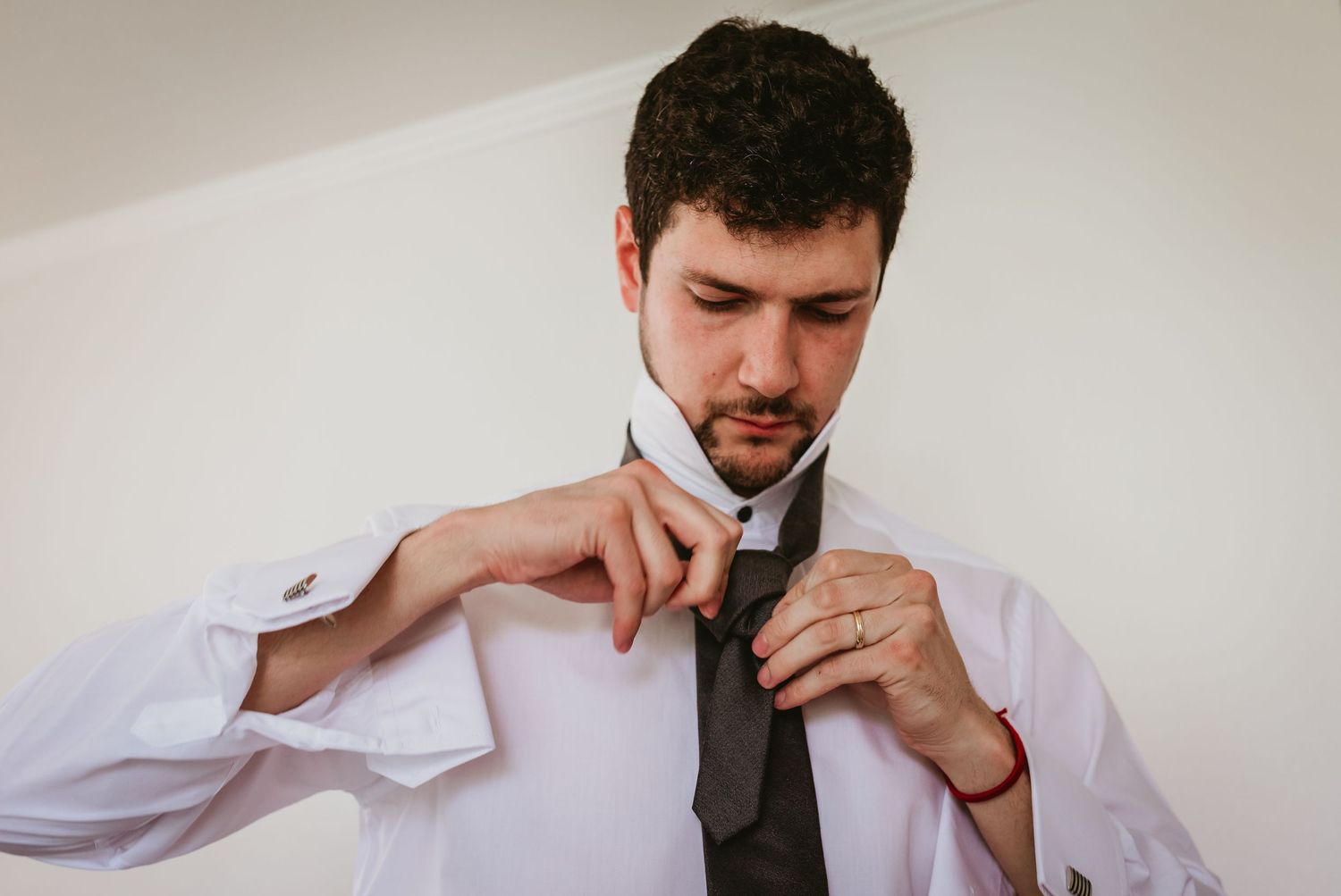 Groom in white dress shirt adjusting his dark tie before wedding ceremony.