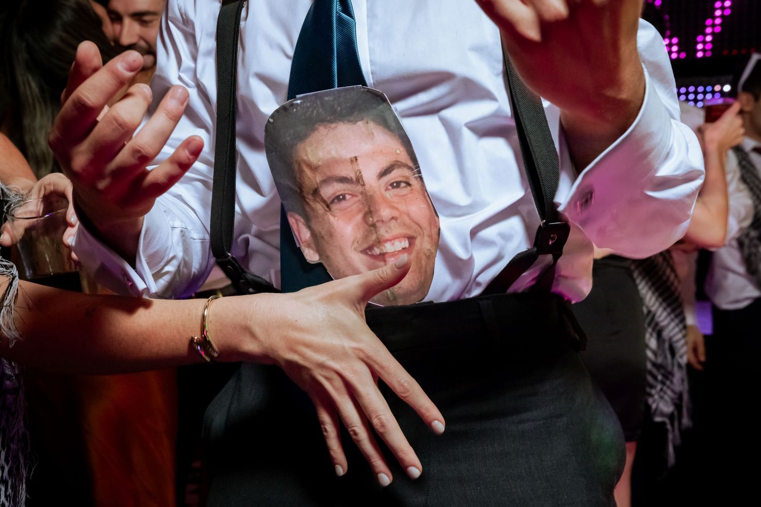 Wedding guest holds up a cardboard face cutout while dancing at a vibrant reception party.