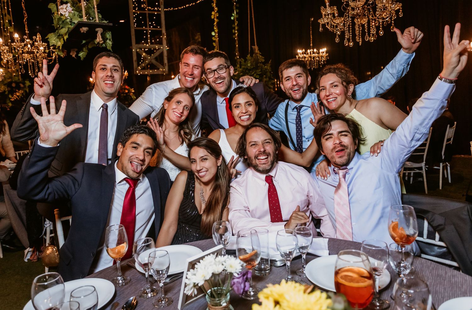 Group of wedding guests celebrating and posing together at decorated reception dinner table.