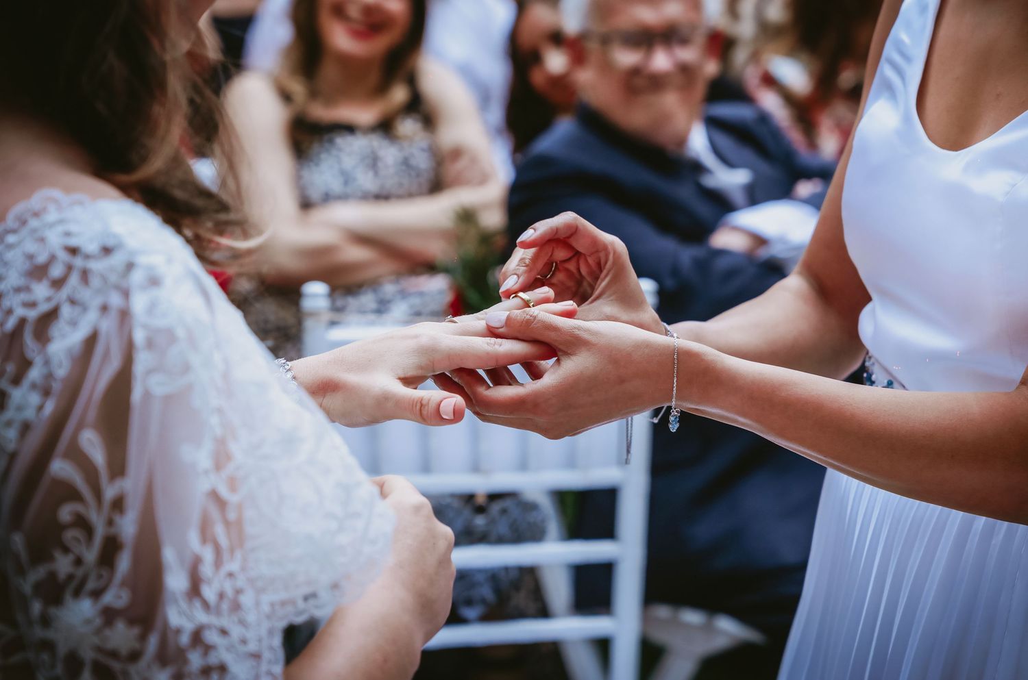Close-up of two brides exchanging wedding rings during an outdoor ceremony.