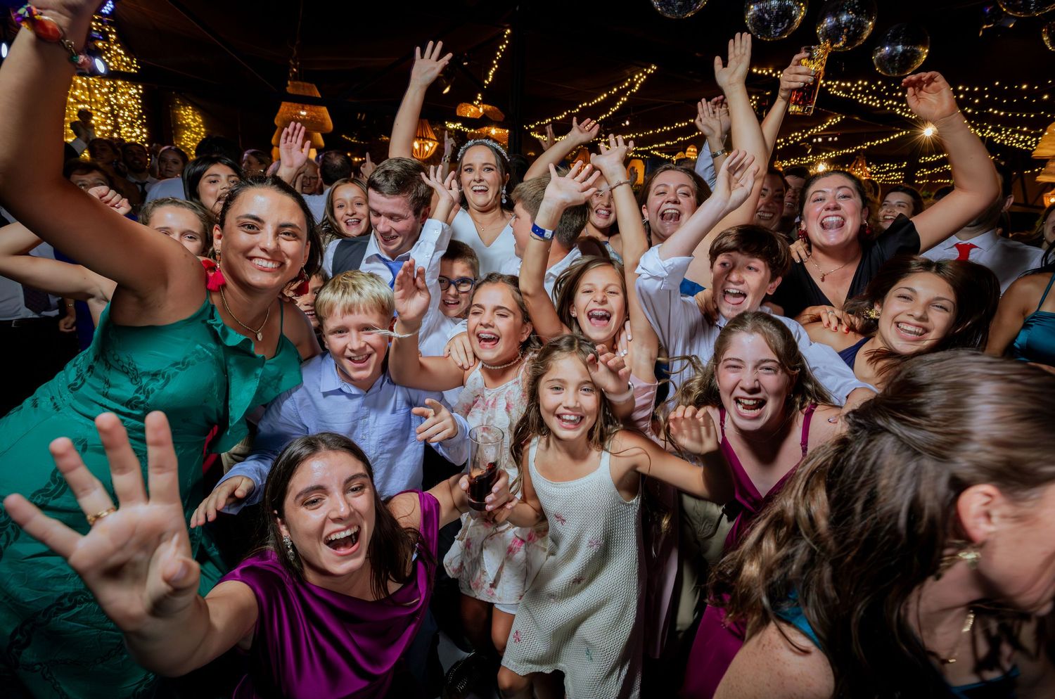 Large group of excited wedding guests including children posing for fun celebratory photo at reception.