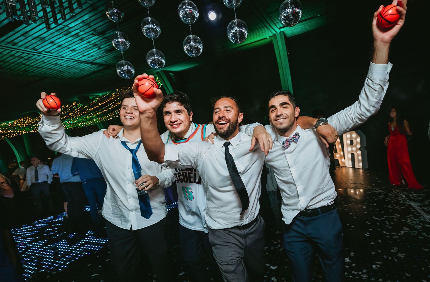 Four friends celebrating at wedding reception holding red apples under disco lights.