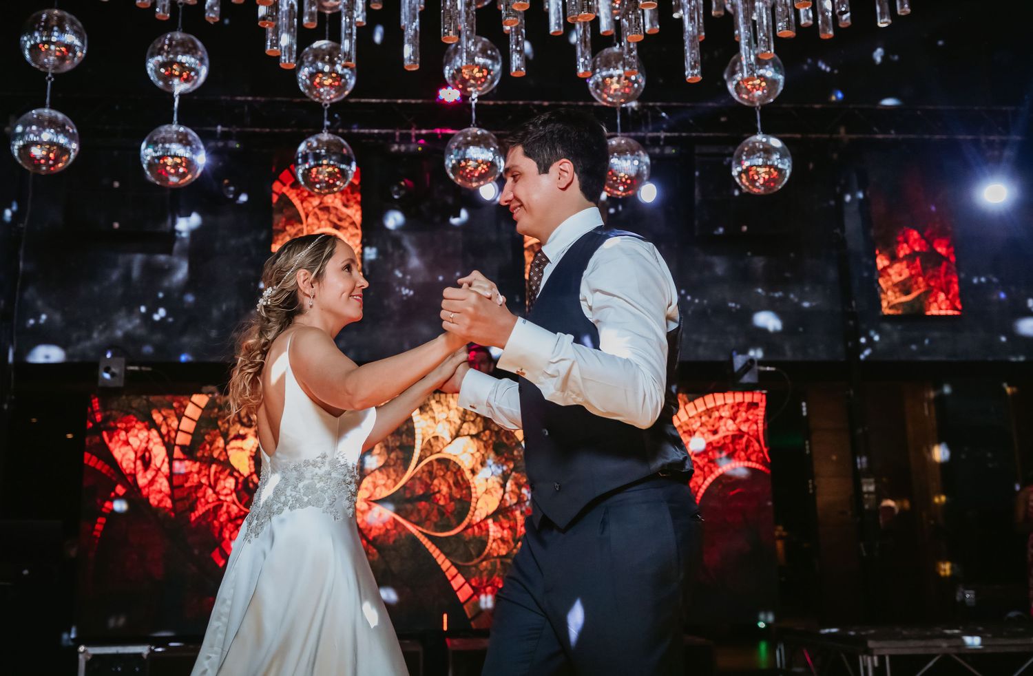 Bride and groom dance joyfully under sparkling disco balls at their glamorous wedding reception venue.