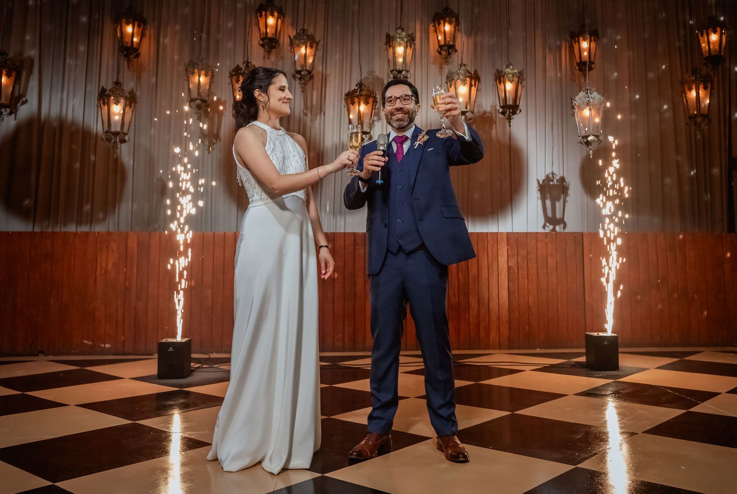 Bride and groom toast with sparklers on checkered dance floor at elegant wedding reception.