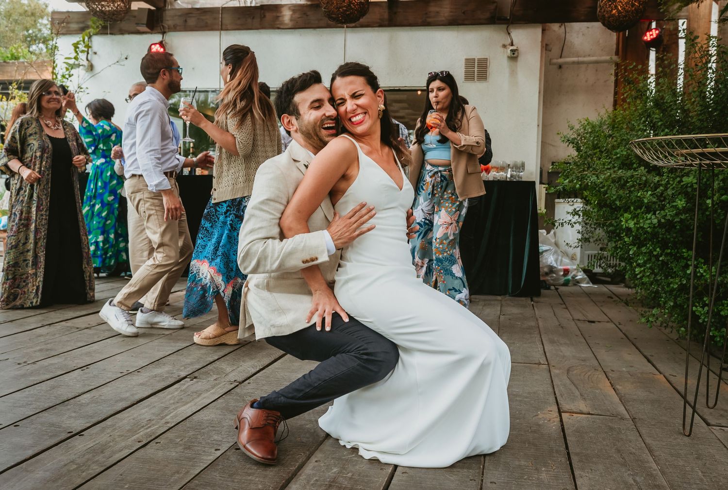 Bride and groom share a joyful dance pose at their outdoor wedding reception with guests celebrating behind them.