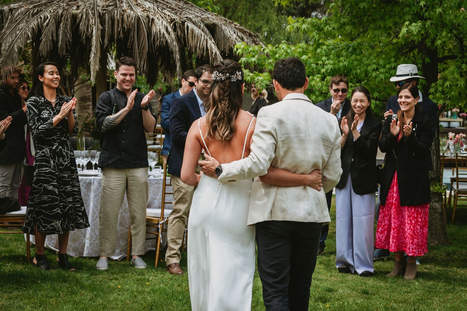 Bride and groom share first dance outdoors at garden wedding while guests clap and celebrate around them.
