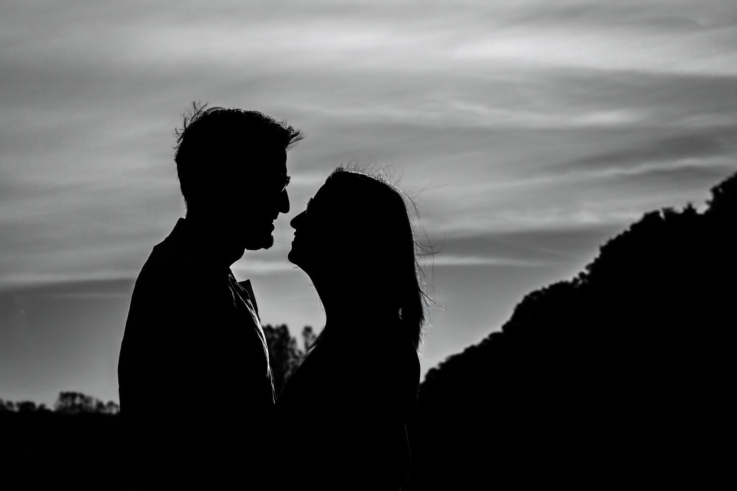 Romantic silhouette of a couple facing each other against a dramatic cloudy sky at sunset.