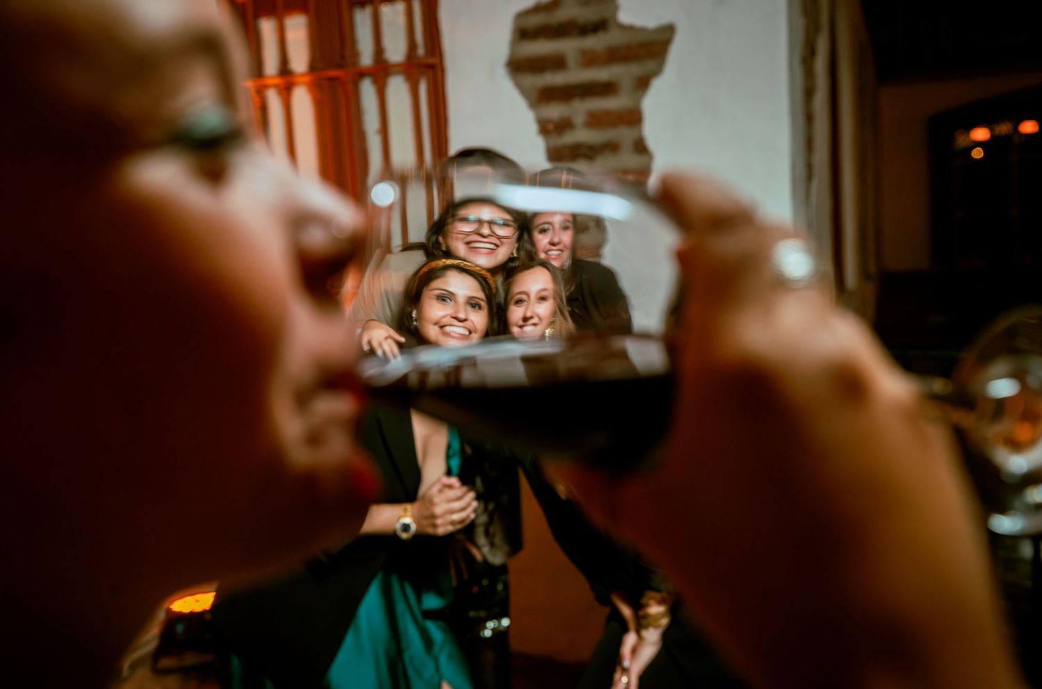 Creative photo of smiling wedding guests reflected in a wine glass at reception.