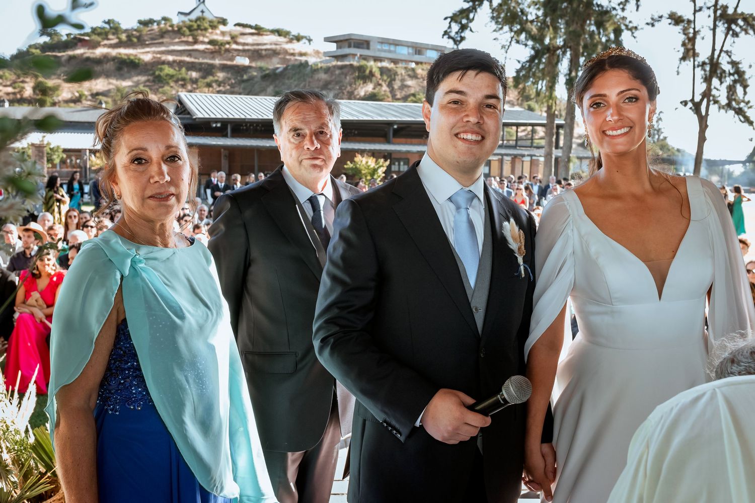 Happy bride and groom pose with family members in formal attire at an outdoor wedding venue.