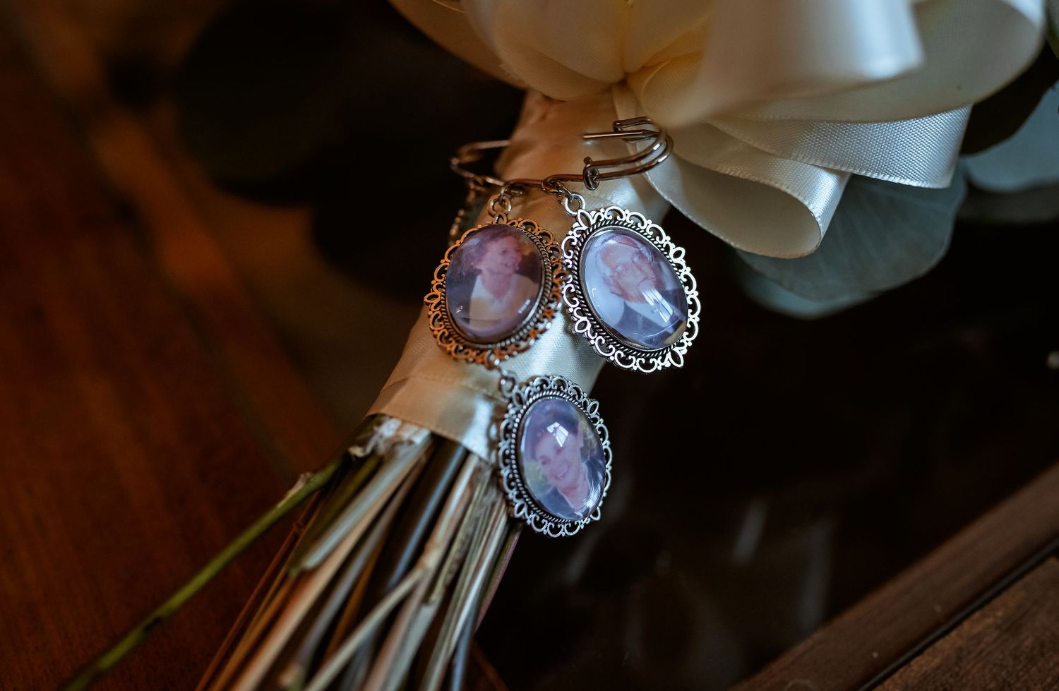 Close-up of three oval photo memorial charms attached to a white wedding bouquet ribbon.