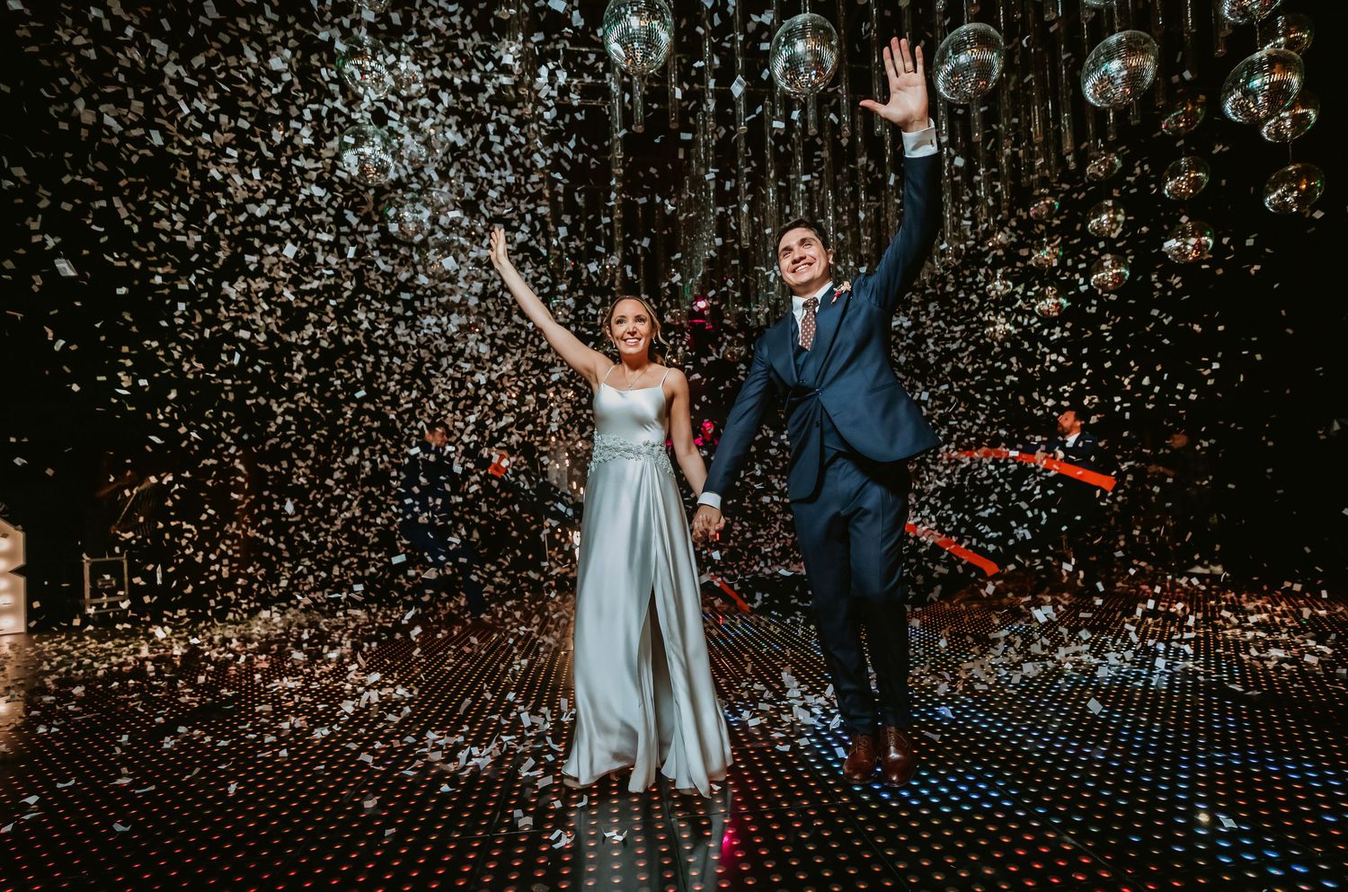 Joyful bride and groom celebrating with confetti under disco balls at a glamorous wedding reception.