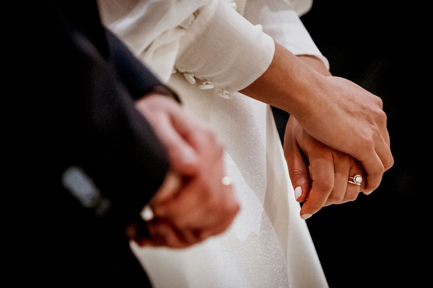 Close-up of a bride and groom holding hands, showcasing a gold wedding ring on the bride's finger.