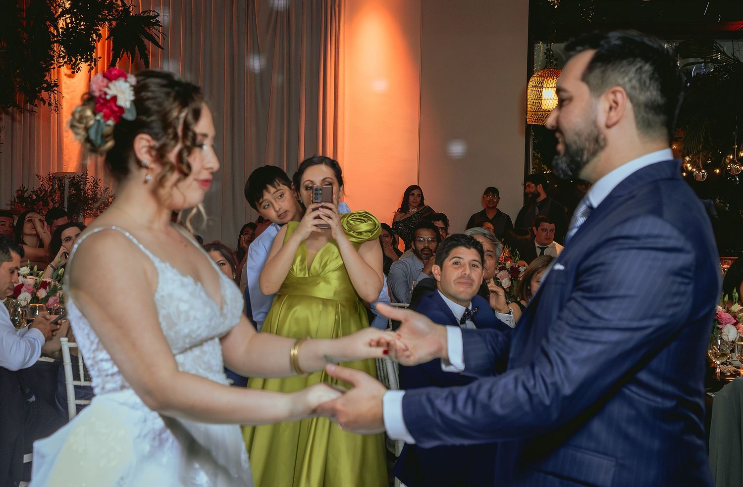 Bride and groom exchange rings during wedding ceremony while bridesmaid in green dress photographs the moment.