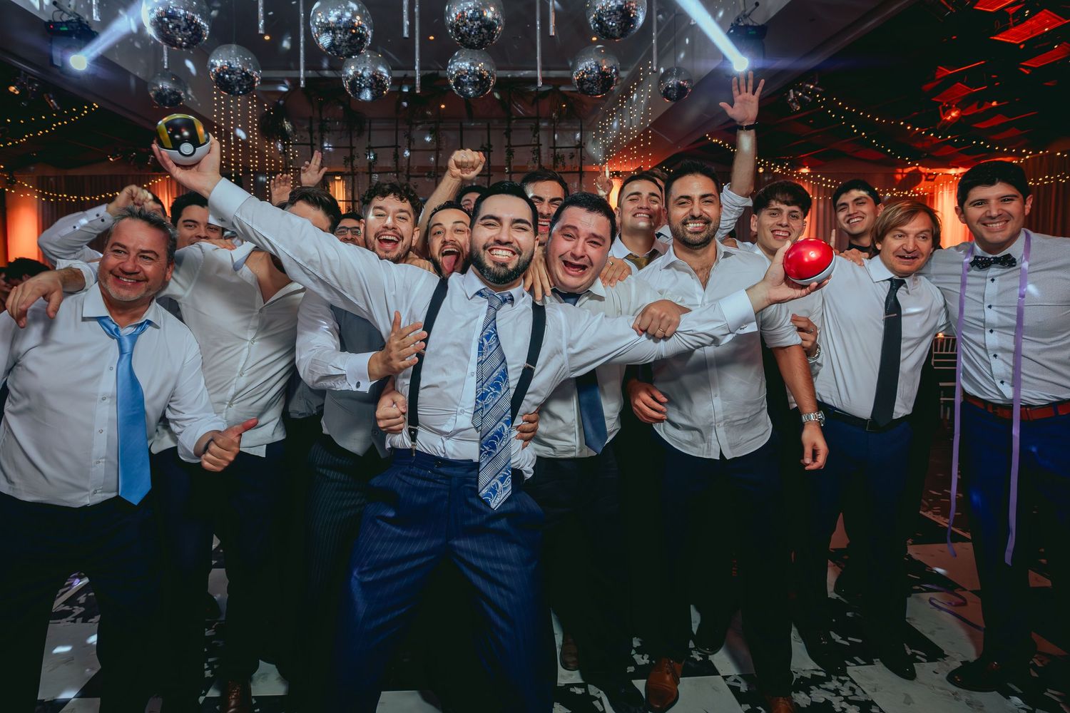 Groom and groomsmen celebrating joyfully on the wedding dance floor under disco balls.