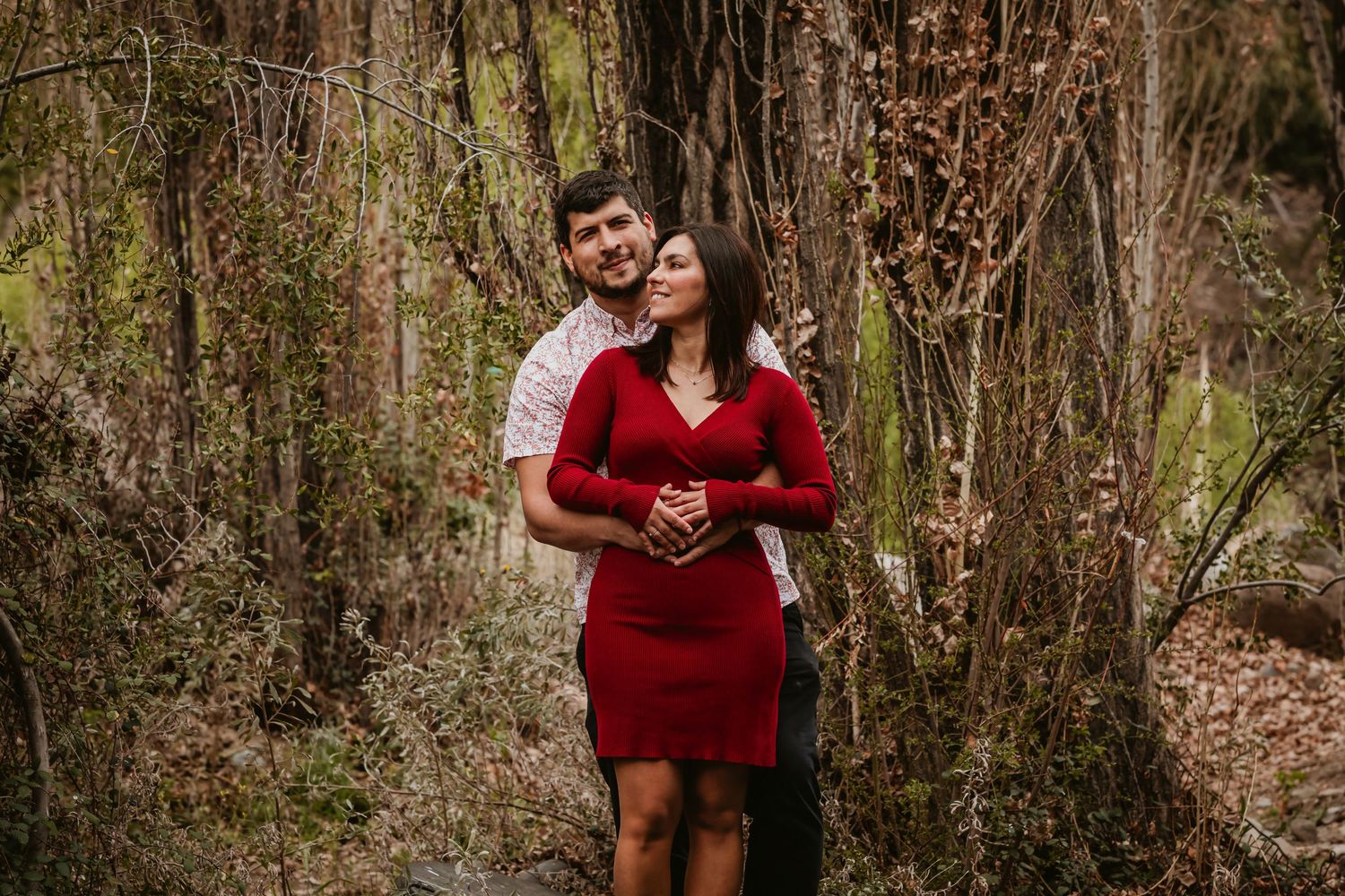 Romantic couple embracing in a wooded forest, woman wearing a red fitted dress.