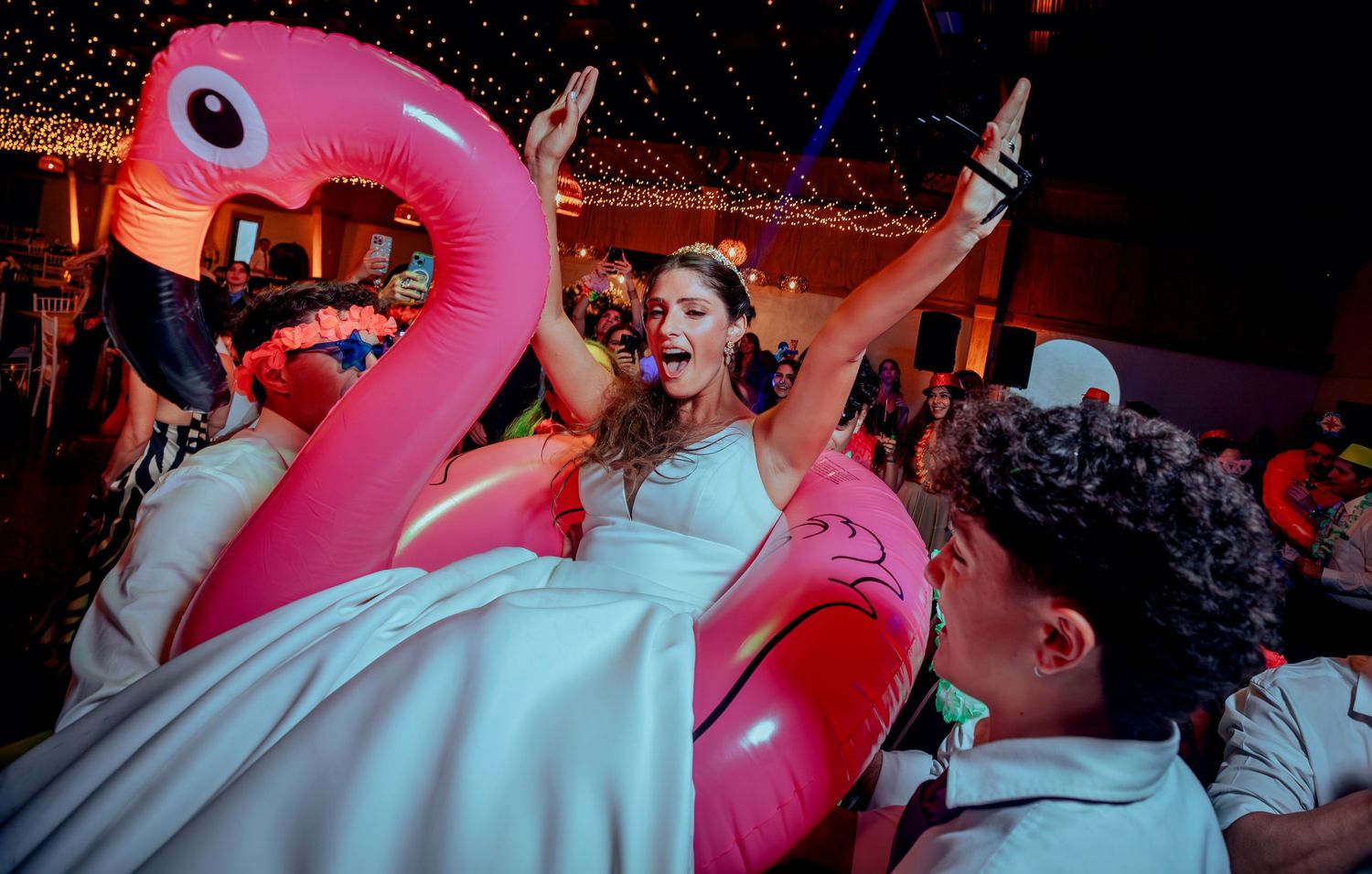 Bride celebrating in pink flamingo inflatable float at wedding reception.