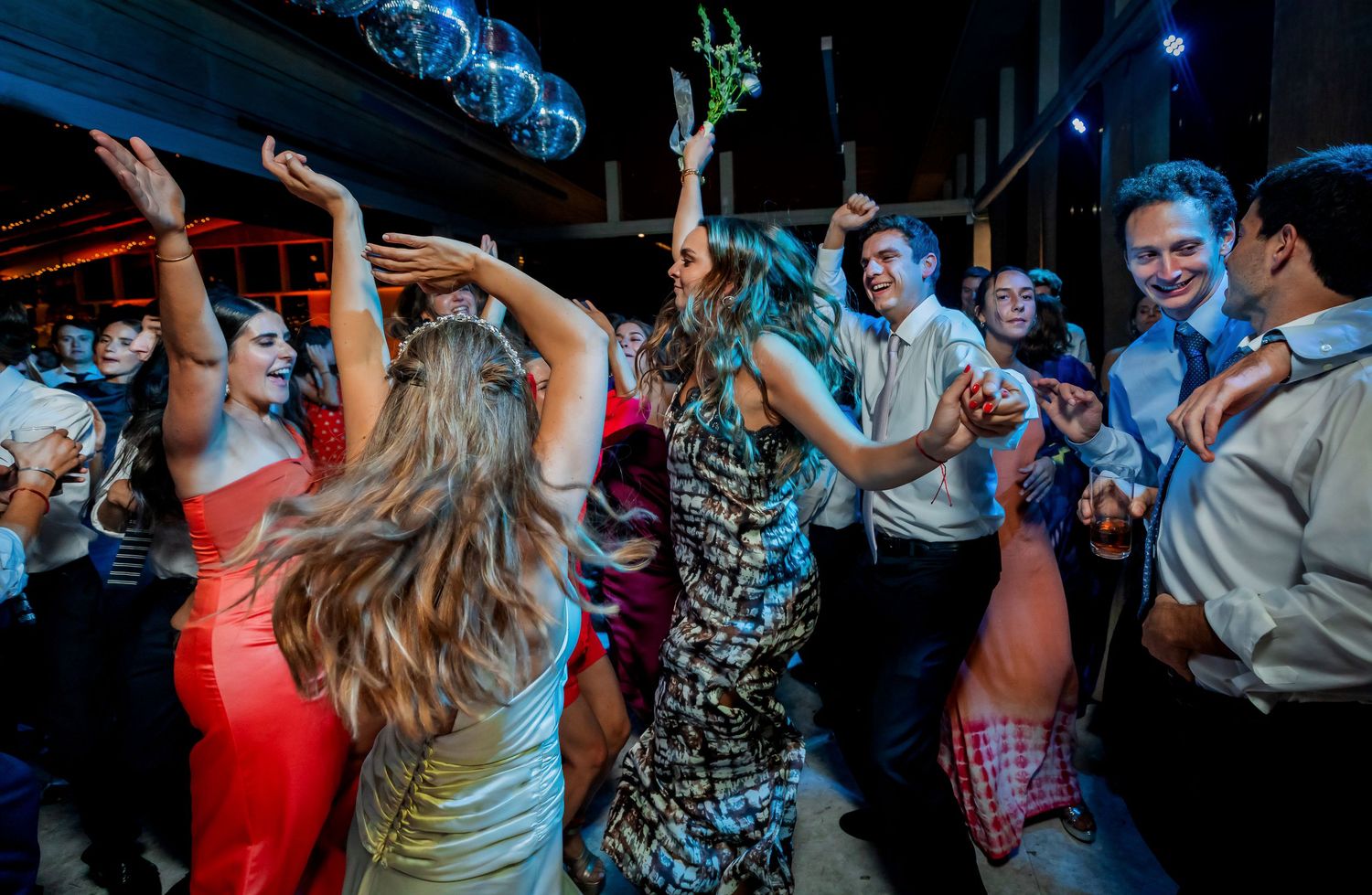 Wedding guests in elegant attire dance joyfully together under disco lights at a festive reception.