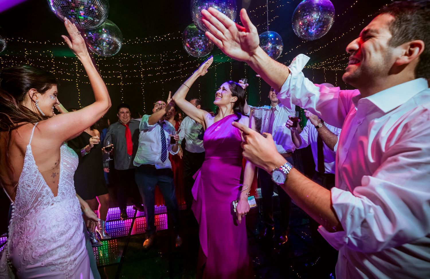 Guests dancing joyfully at a wedding reception with disco balls and colorful lights on the dance floor.