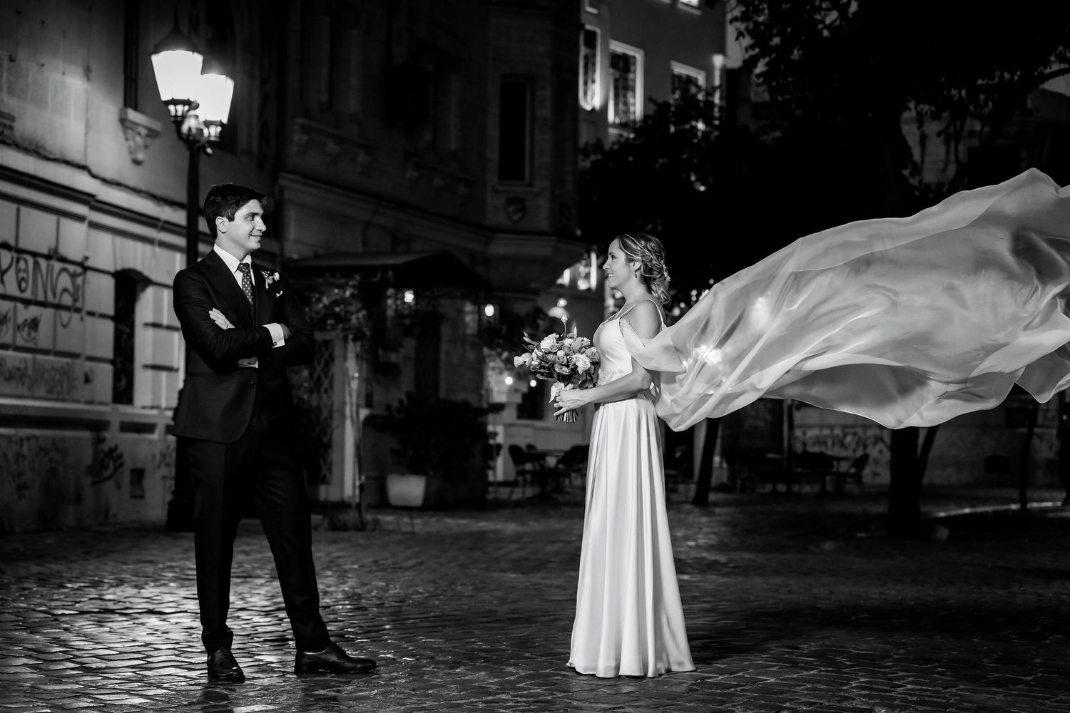 Black and white wedding photo of bride and groom on cobblestone street at night.