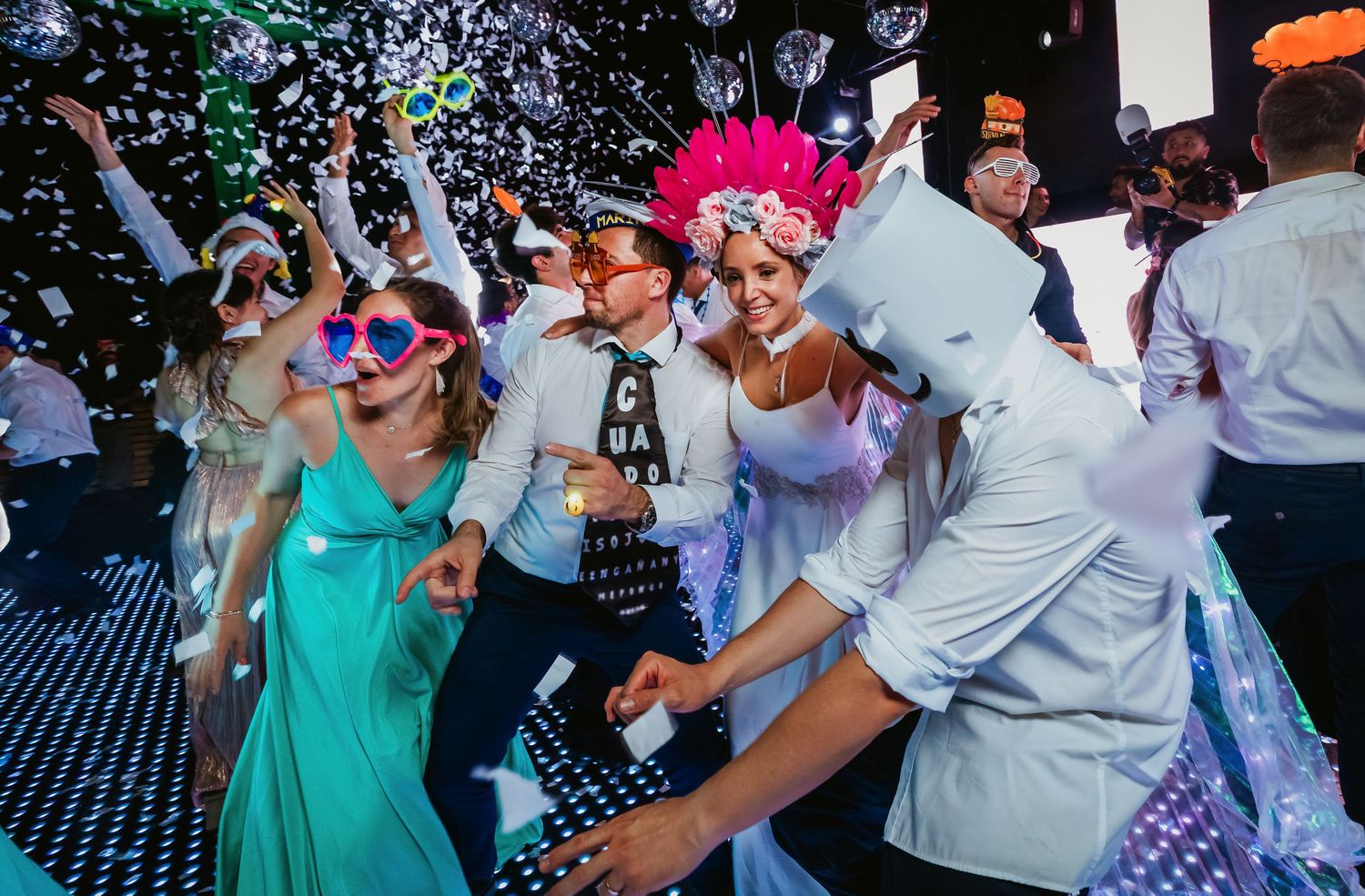 Wedding guests celebrate with confetti, fun props and costumes on a sparkling dance floor at lively reception.