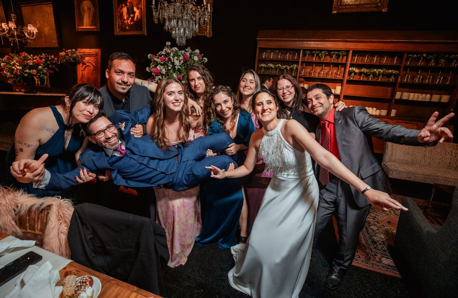 Bride and groom celebrate with smiling wedding guests in cozy bar lounge setting.