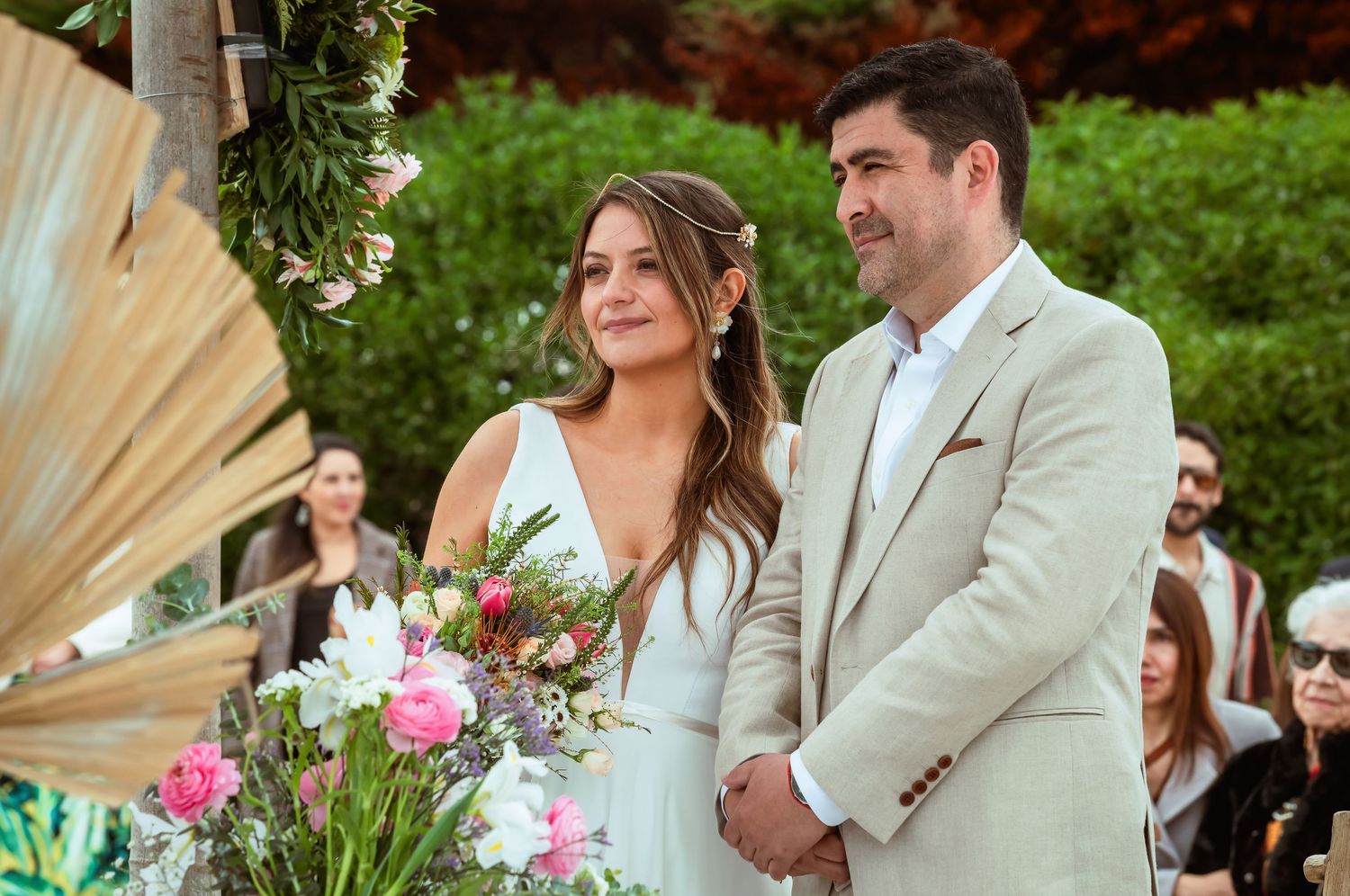 Bride and groom stand together at outdoor wedding altar surrounded by tropical floral arrangements.