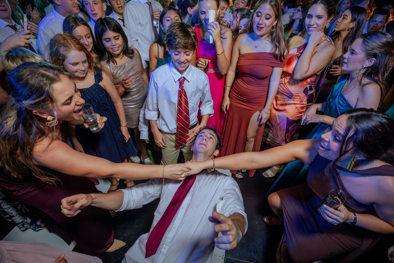 Wedding guests enthusiastically dancing as a man in a red tie leans back surrounded by cheering crowd.