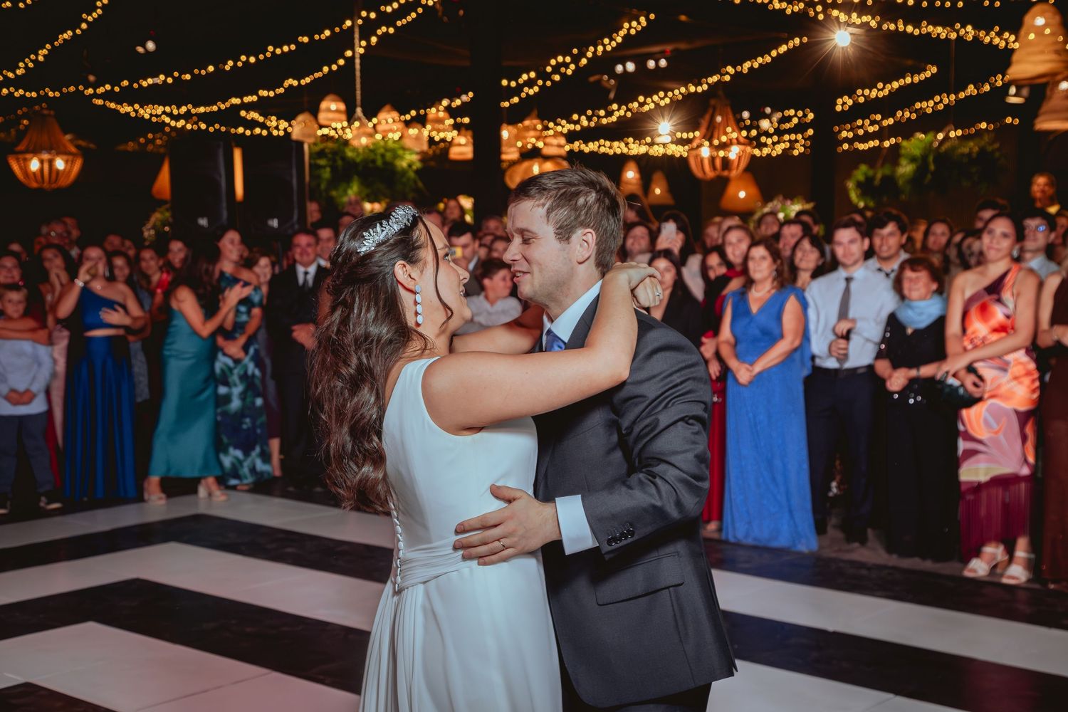 Bride and groom share romantic first dance embrace at elegant outdoor wedding reception with string lights.