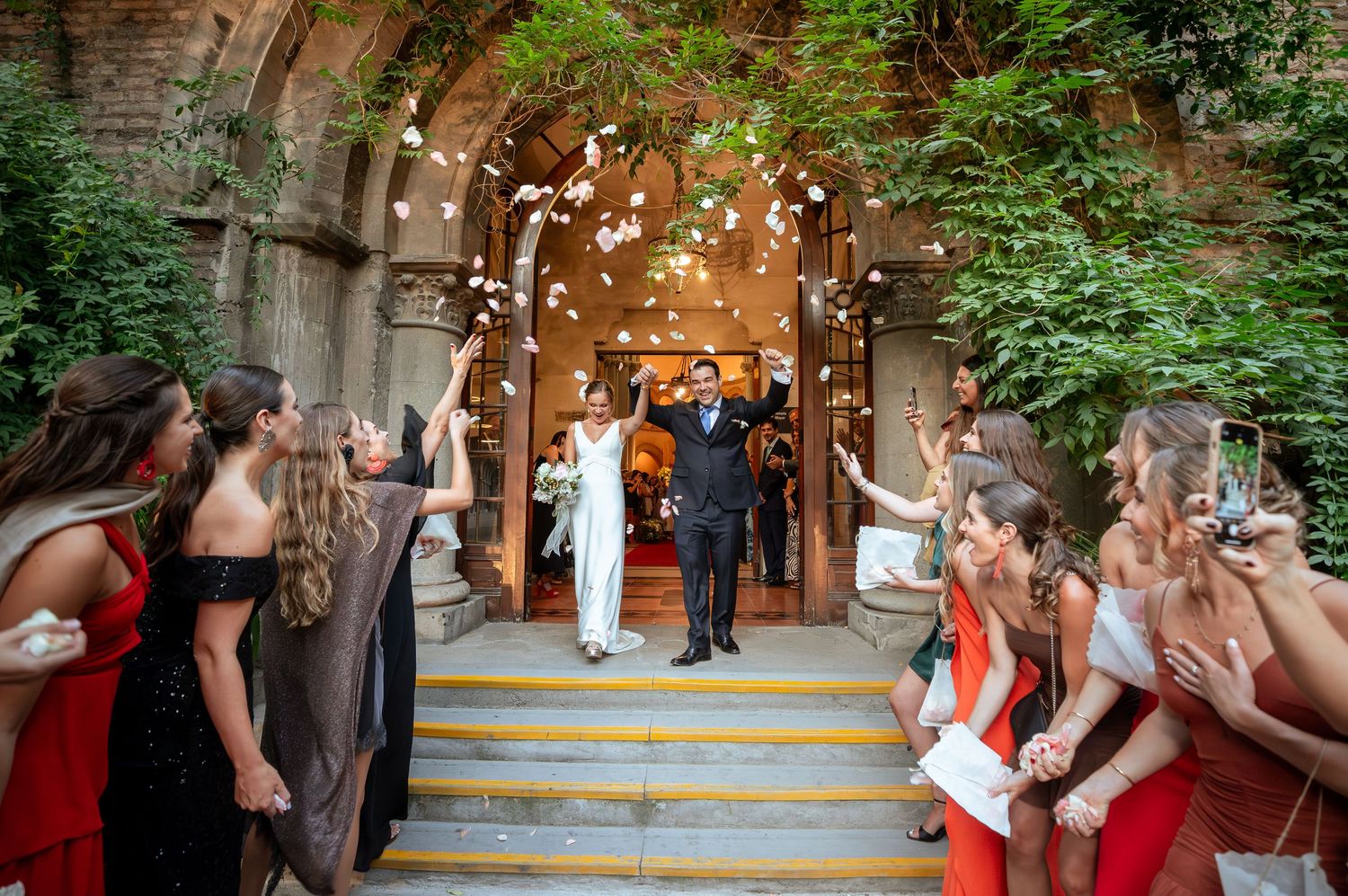 Newlyweds exit historic stone church entrance as guests throw flower petals in celebration.
