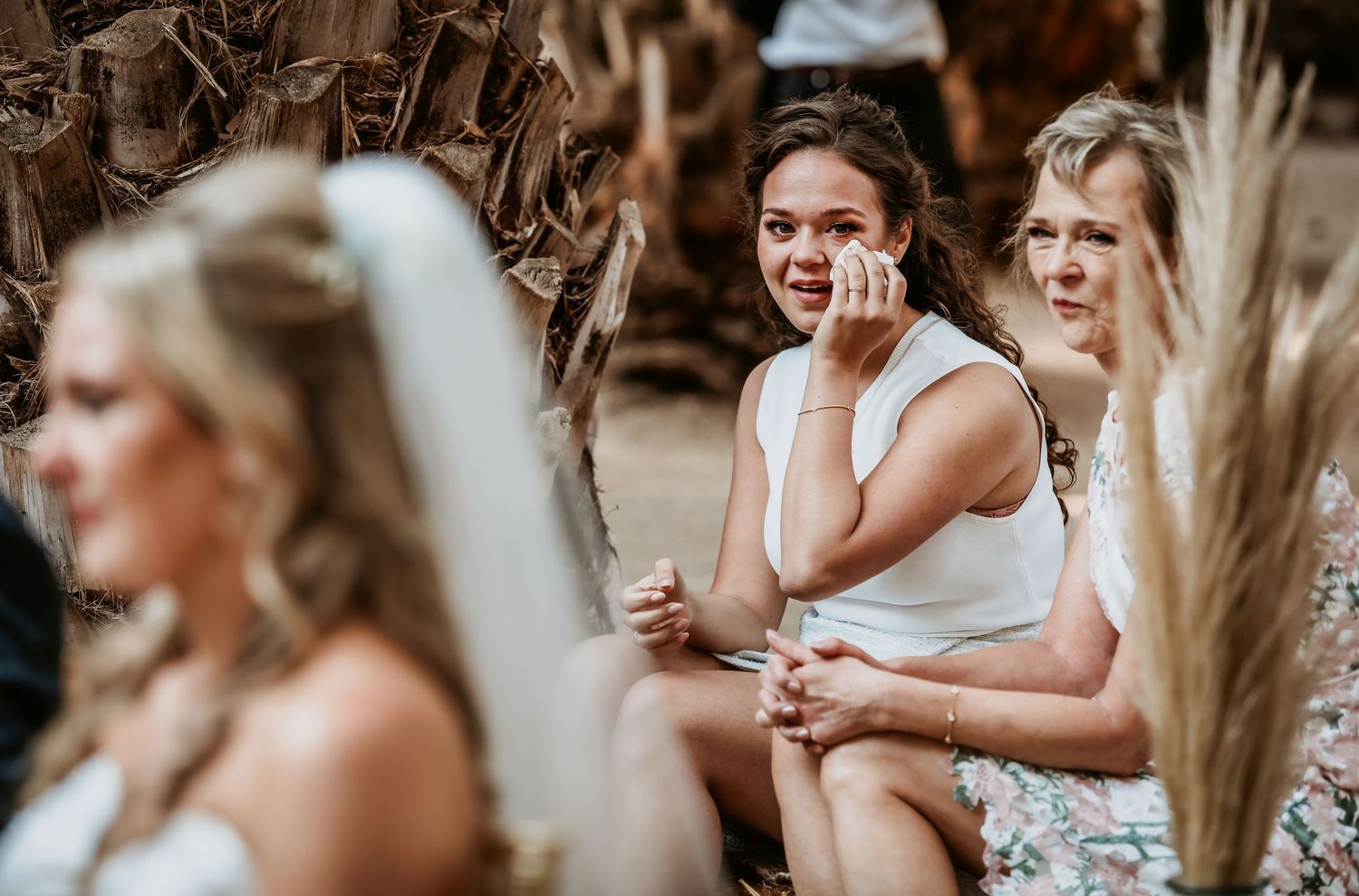 Emotional wedding guest wipes tears while seated during touching outdoor wedding ceremony.