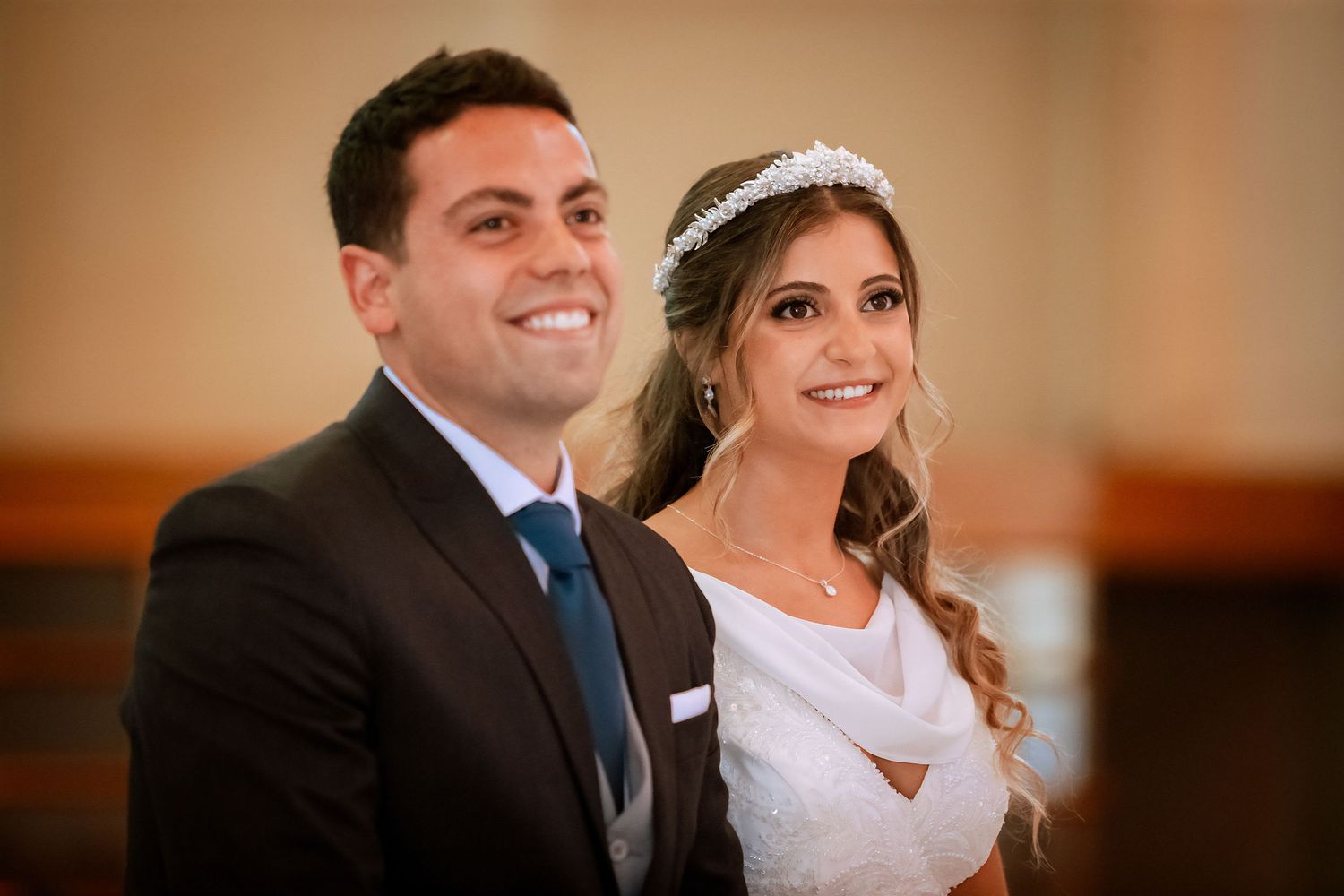 Smiling bride and groom portrait during wedding ceremony inside a church, bride wearing tiara and white gown.