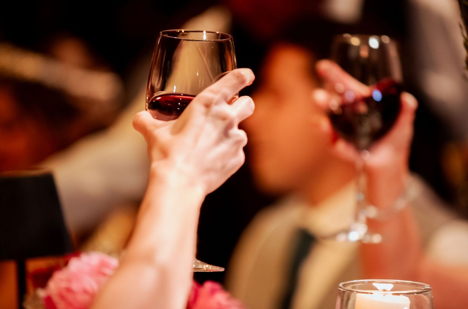 Guests raise glasses of red wine in a celebratory toast at an elegant wedding reception.