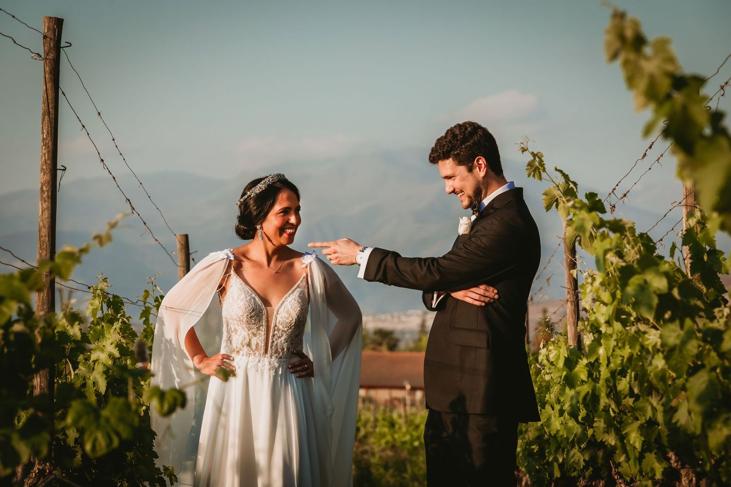 Smiling bride and groom share a joyful moment together in a vineyard with mountain views.
