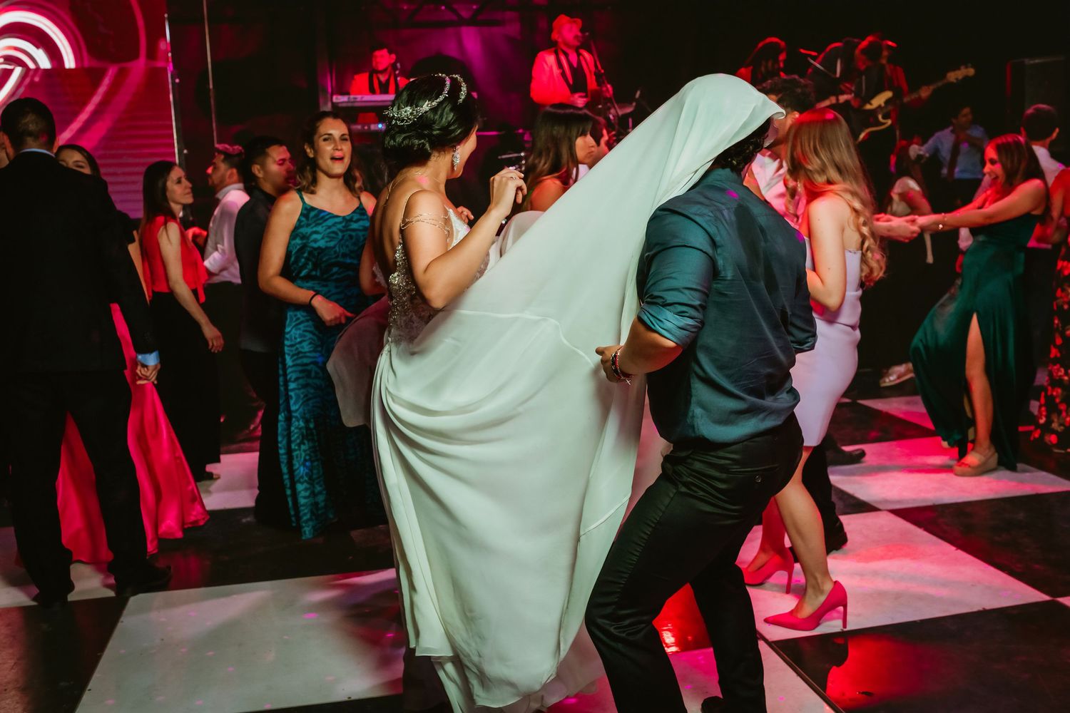 Bride in white gown dancing with a guest on a checkered wedding reception dance floor.