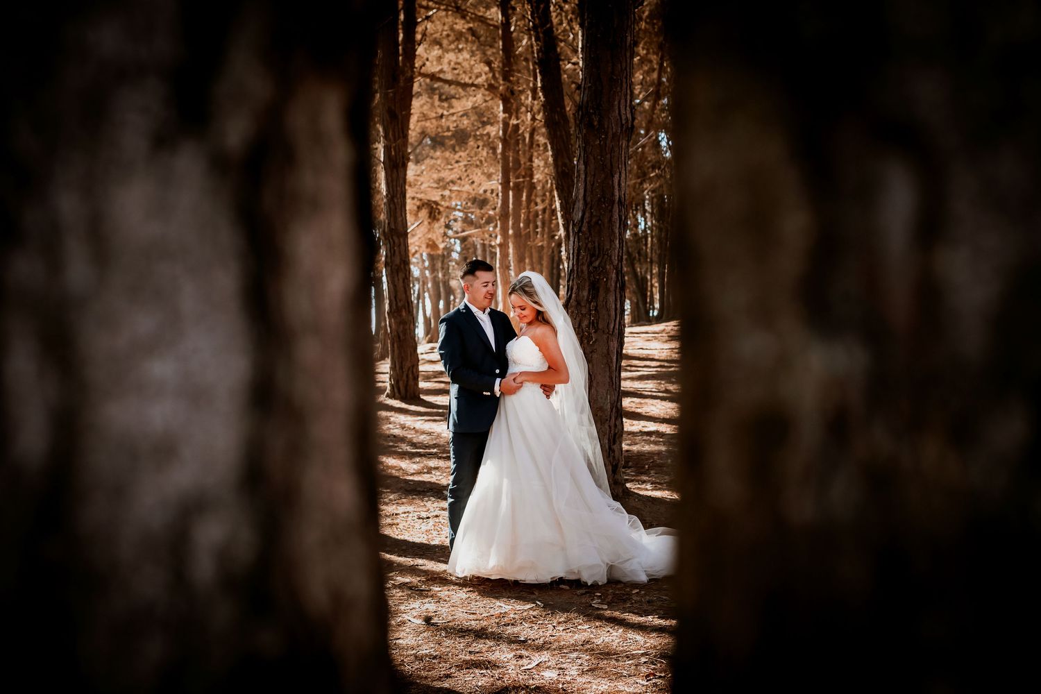 Bride and groom sharing a romantic moment framed by forest trees.