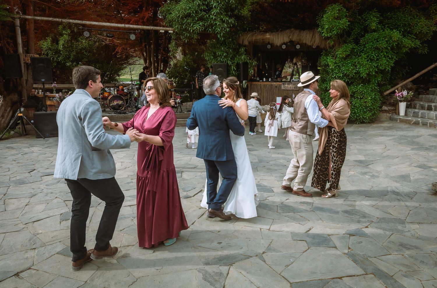 Wedding guests dancing in pairs on a stone patio while the bride and groom share a dance at their reception.