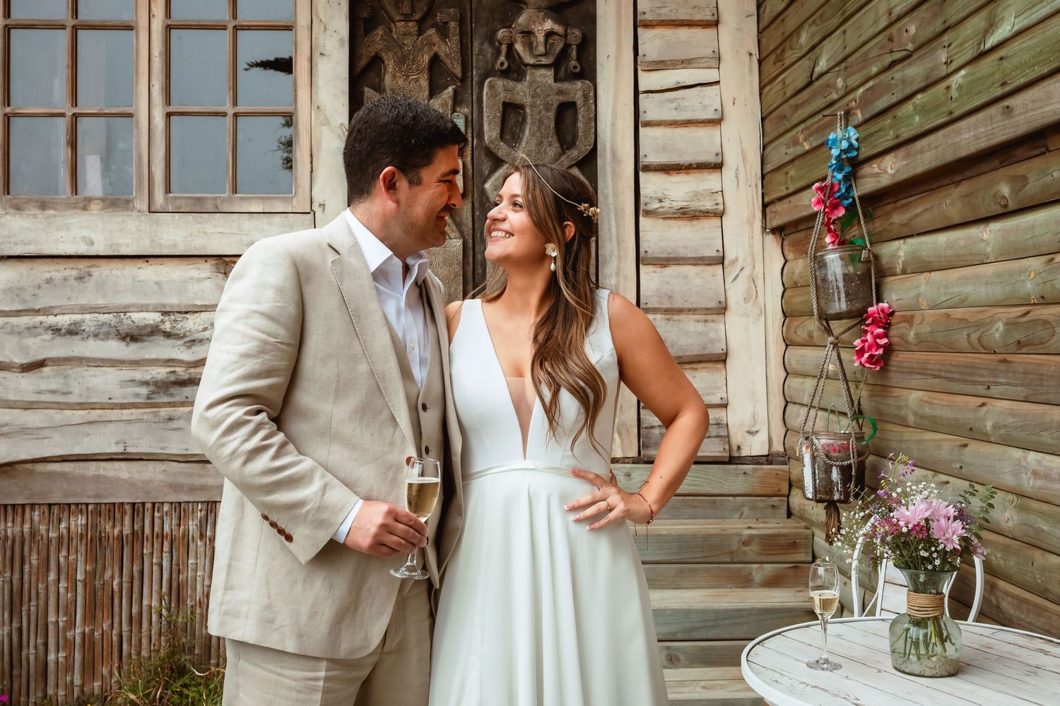 Newlyweds share a romantic moment on a rustic wooden porch holding champagne glasses at their wedding.