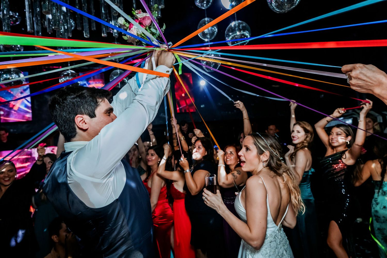 Wedding guests dancing with colorful ribbon streamers under disco balls.