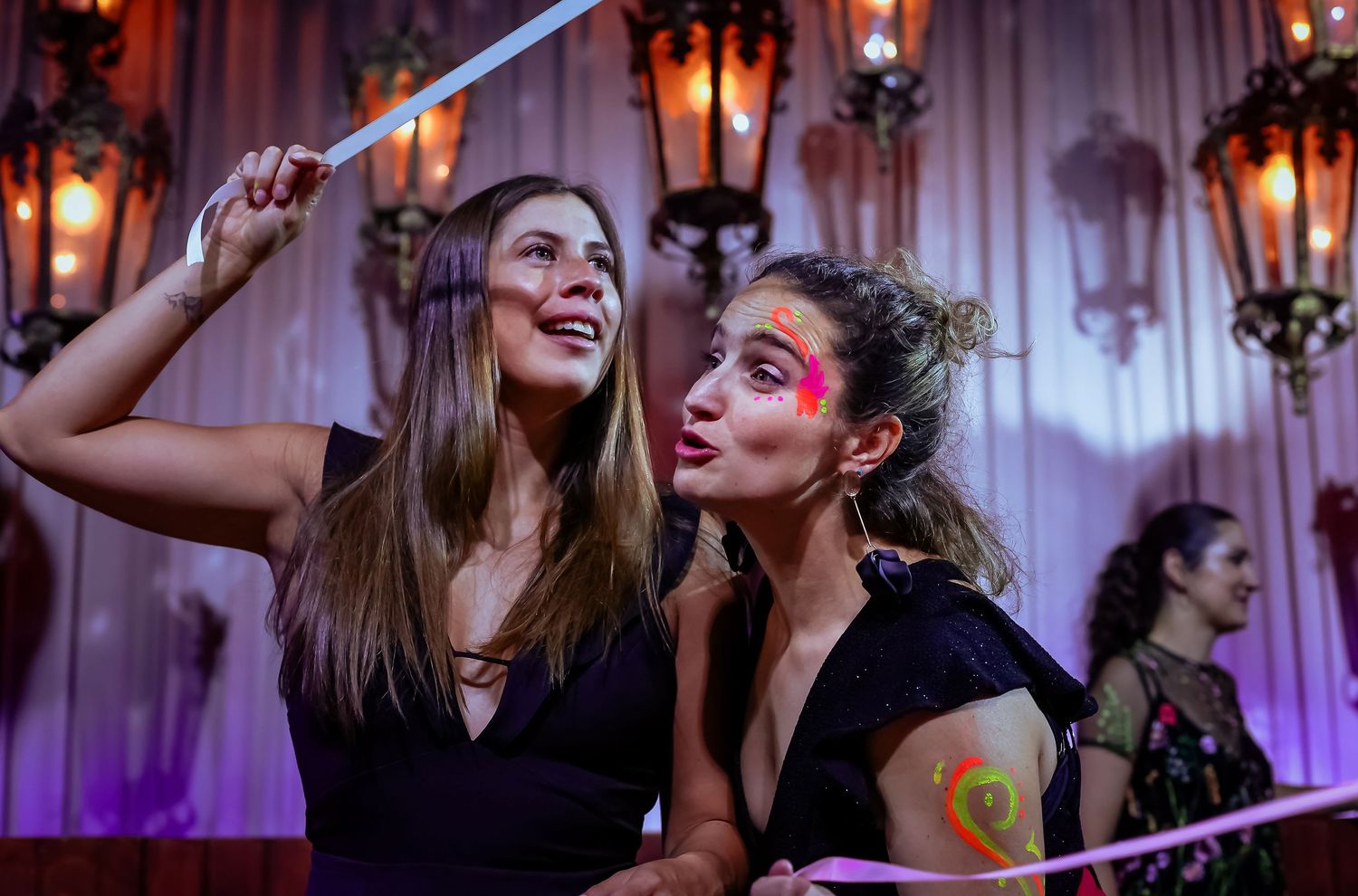 Two women smile and pose with a light-up wand at a colorful evening celebration event.