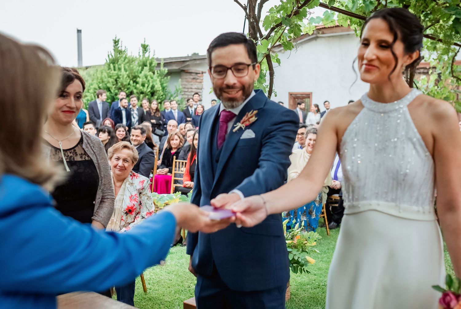 Bride and groom receive rings from officiant at outdoor wedding ceremony.