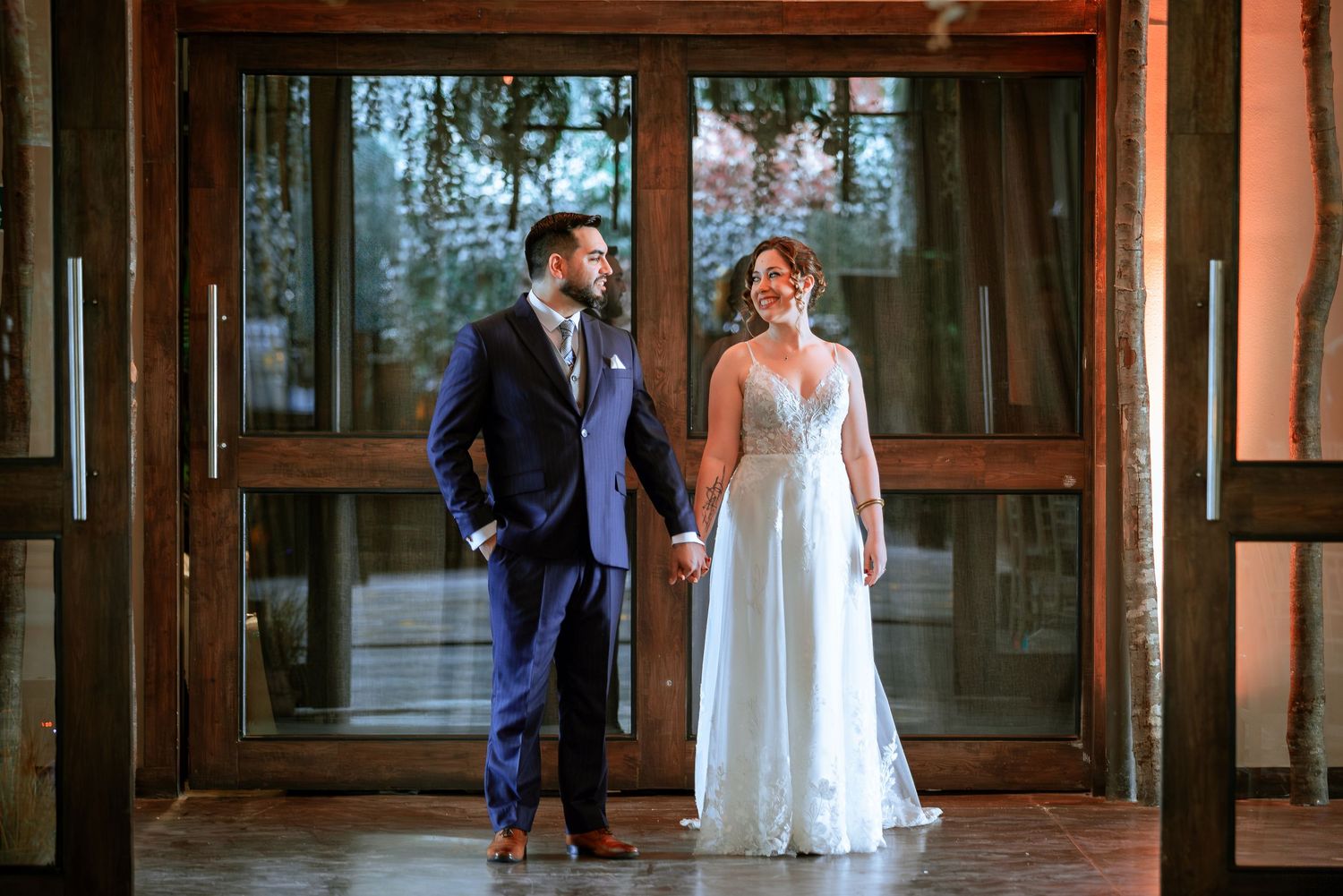 Bride and groom hold hands while posing in front of grand wooden doors at their wedding venue.