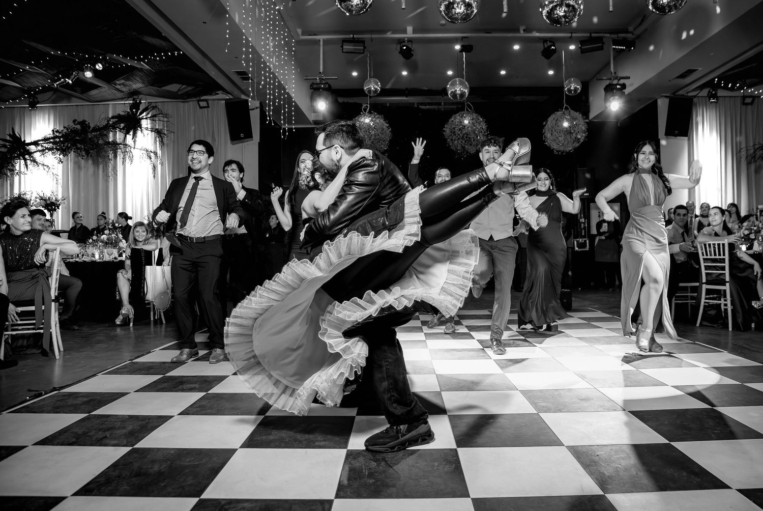 Dramatic dip move performed by dancers on checkered floor at elegant wedding reception celebration.