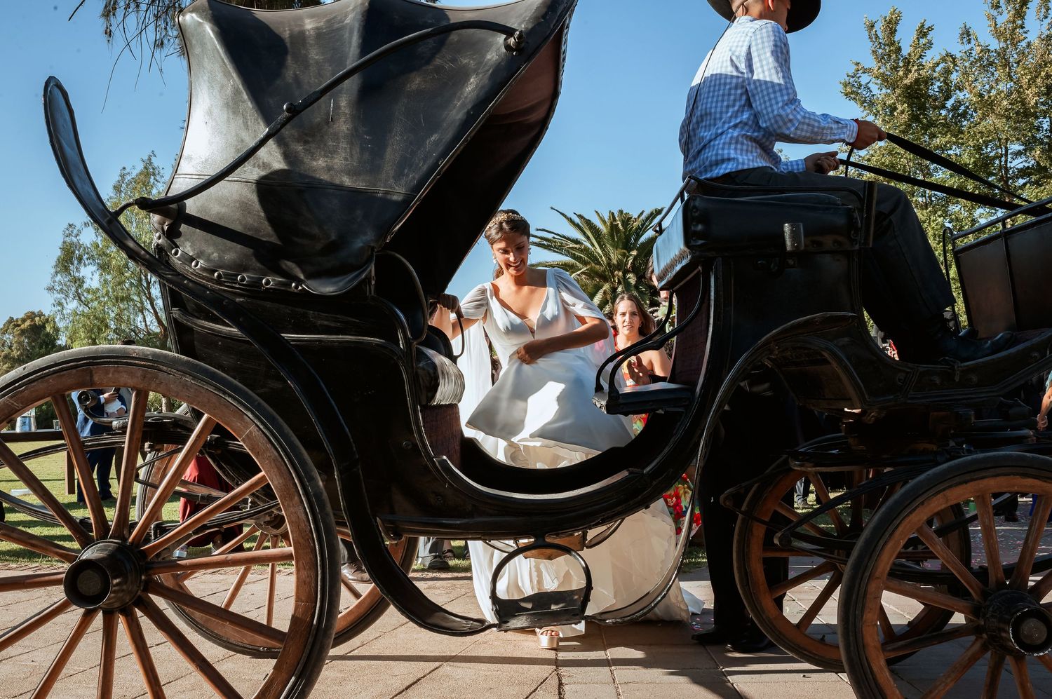 Elegant bride riding in vintage black horse-drawn carriage on wedding day.