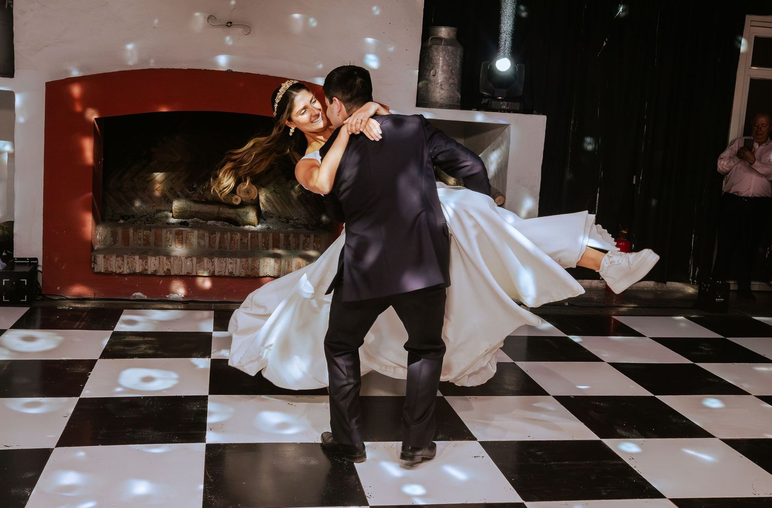 Groom sweeps bride off her feet during elegant first dance on black and white floor.