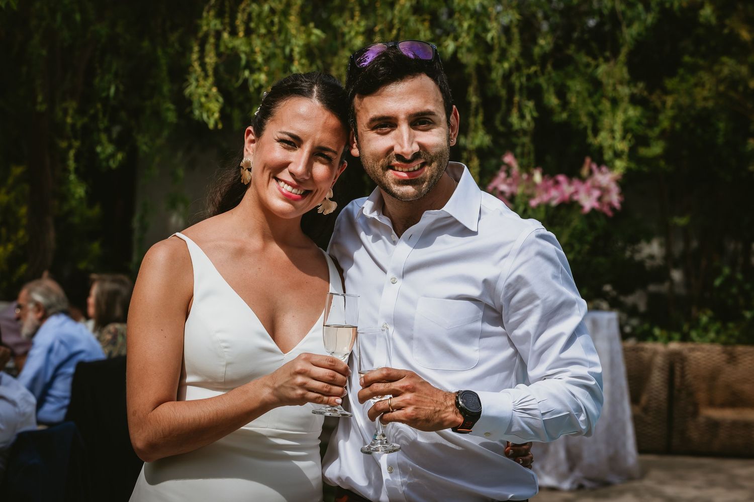 Couple smiling and toasting with champagne glasses at an outdoor wedding reception.