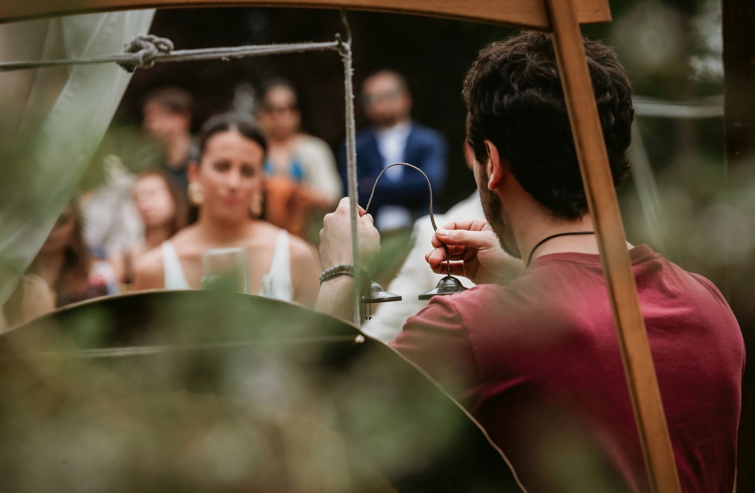 Man holding a wine glass viewed from behind at an outdoor wedding reception with guests in background.