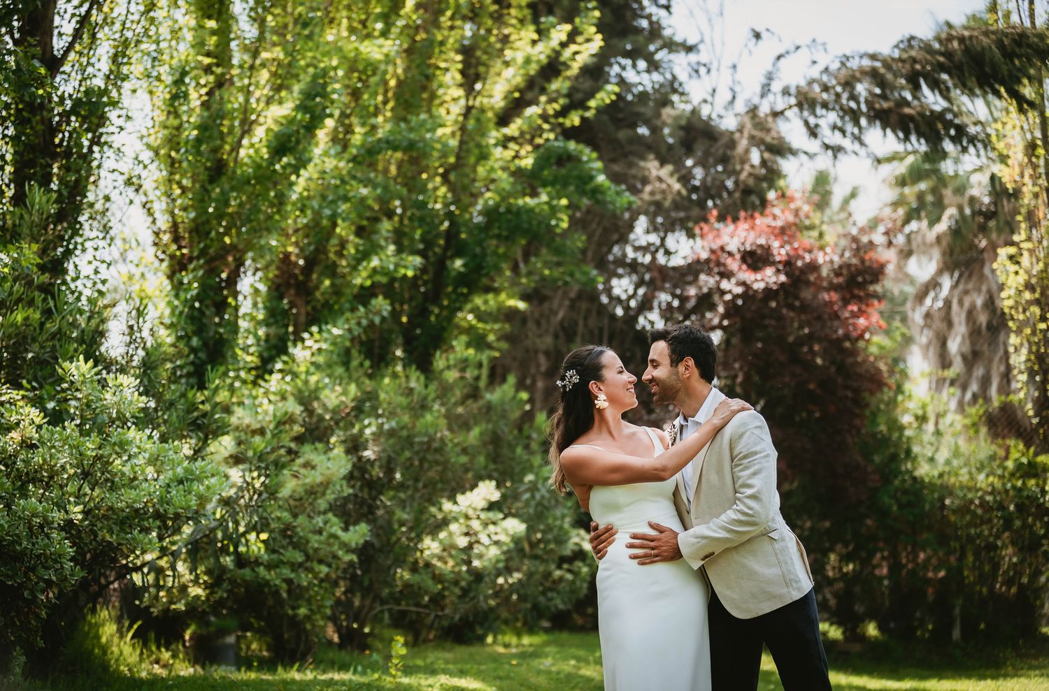 Bride and groom embracing in a lush garden, sharing a romantic moment on their wedding day.